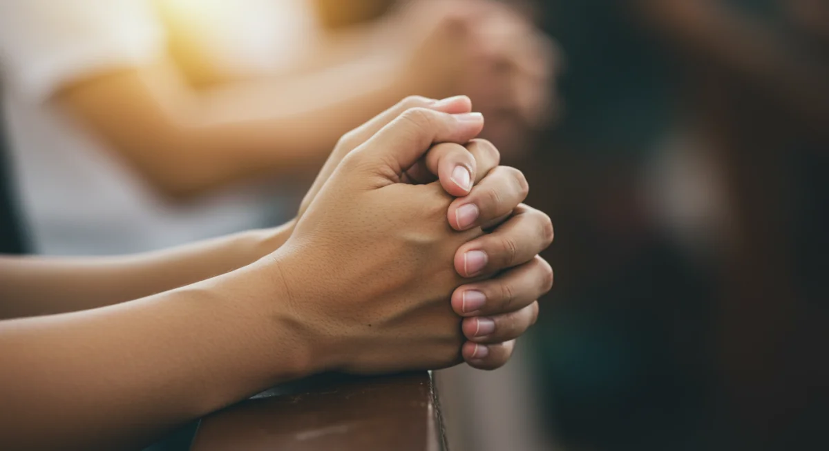 Mãos unidas em oração com um brilho suave, representando conexão espiritual e força na fé.