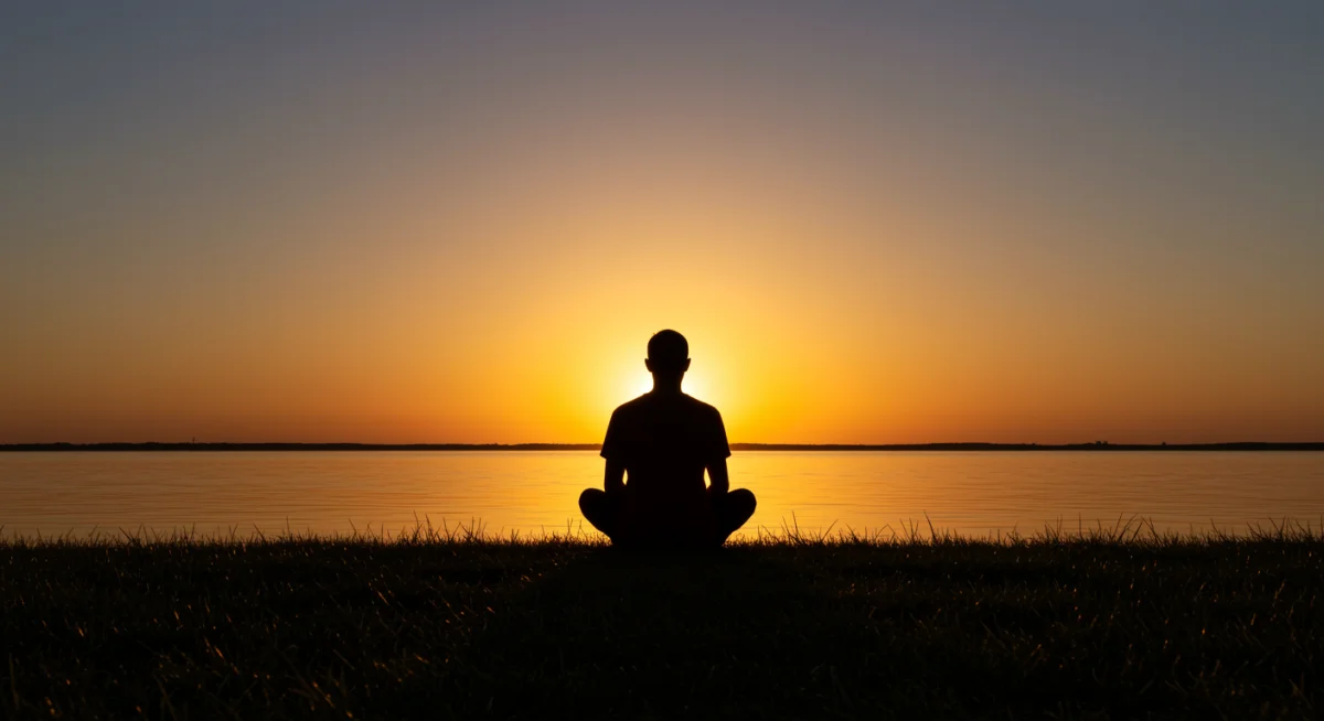 Pessoa meditando ao amanhecer em um lago, simbolizando renovação e tranquilidade.