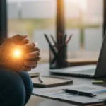 Pessoa orando ajoelhada em um ambiente de escritório, buscando orientação divina para o trabalho e sucesso profissional.