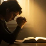 Pessoa orando de joelhos com as mãos postas, silhueta contra uma luz acolhedora, simbolizando esperança e conexão divina em tempos de aflição.