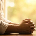 Pessoa orando ajoelhada, envolvida por uma luz suave e calorosa, simbolizando cura e esperança.